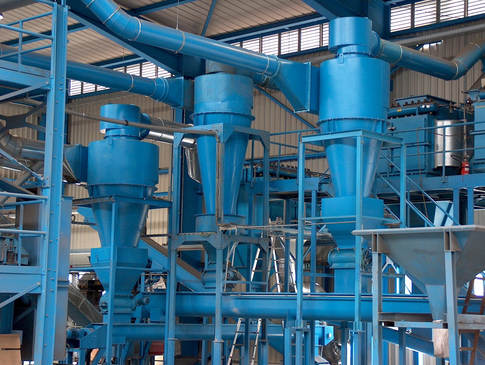 Mehrere blau lackierte WALTER Zyklonabscheider in einer Produktionshalle, verbunden über Wickelfalzrohre mit Beruhigungsbehältern unter den Trichtern